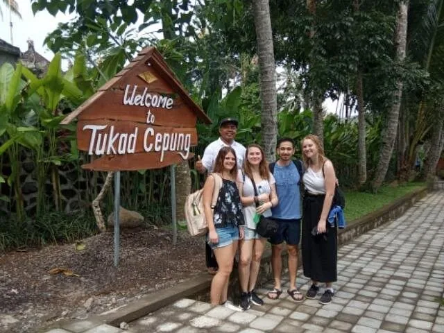 A group of tourists poses by the Welcome to Tukad Cepung sign.