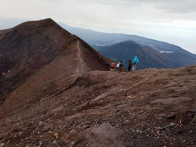 A group of hikers ascends a steep rocky ridge on Mount Agung.