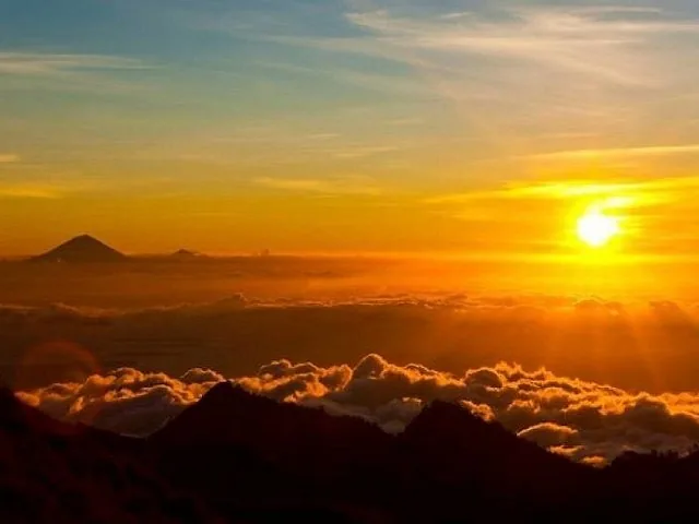 A golden sunrise over a sea of clouds with mountain peaks emerging.