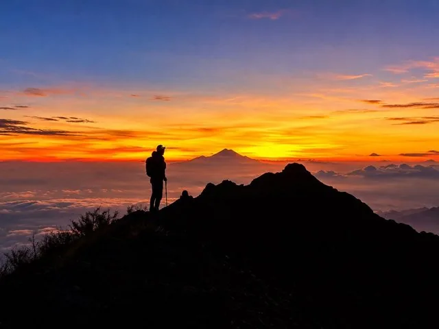 Silhouette of a hiker on a mountain peak at sunrise over clouds.