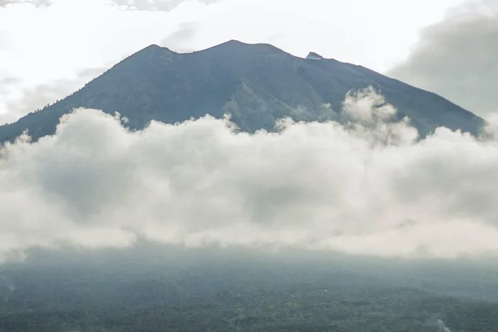 Mount Agung towers above thick white clouds under an overcast sky.