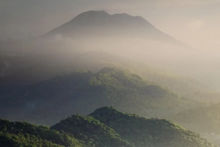 A misty, layered mountain landscape with Mount Agung visible in the distance.