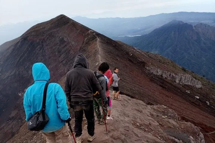 Hikers walk in single file along a steep, narrow mountain ridge.