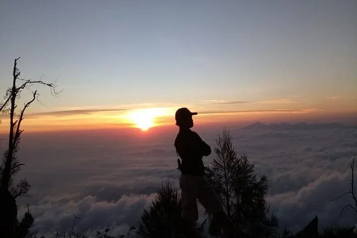 Silhouette of a person standing on a mountain peak at sunrise.